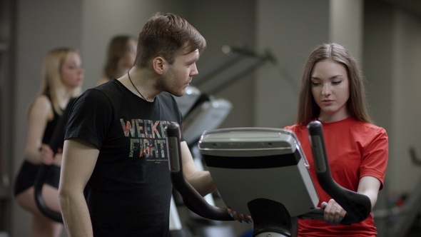 Lovely Girl in Red Shirt Vigorously Work on Exercise Bike and Trainer Come Help with Motivation Her