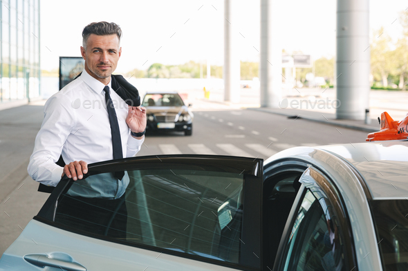 Smiling mature businessman getting in taxi outside Stock Photo by vadymvdrobot