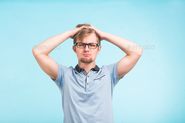Puzzled hesitant male put his hands on head against blue background. Stock Photo by Satura_
