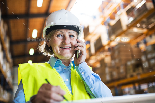 Senior woman warehouse manager or supervisor with smartphone, making phone call. Stock Photo by halfpoint