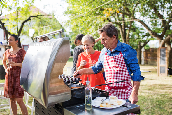 A senior man cooking food on the grill on a barbecue party outside in the backyard. Stock Photo by halfpoint