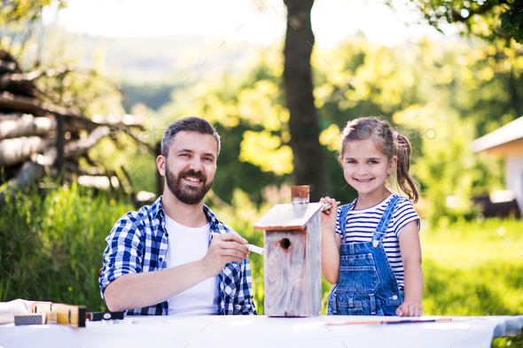 Father with a small daughter outside, painting wooden birdhouse. Stock Photo by halfpoint