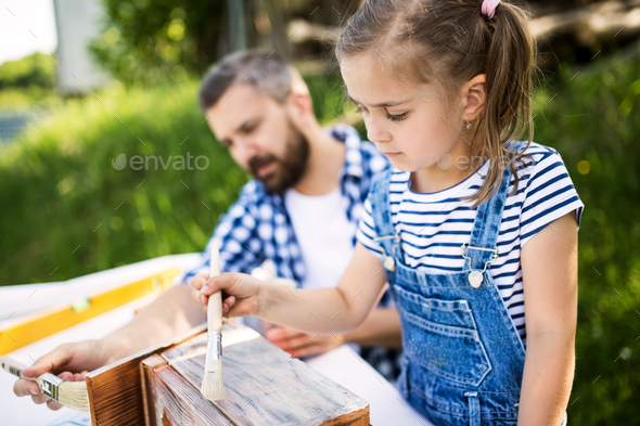 Father with a small daughter outside, painting wooden birdhouse.