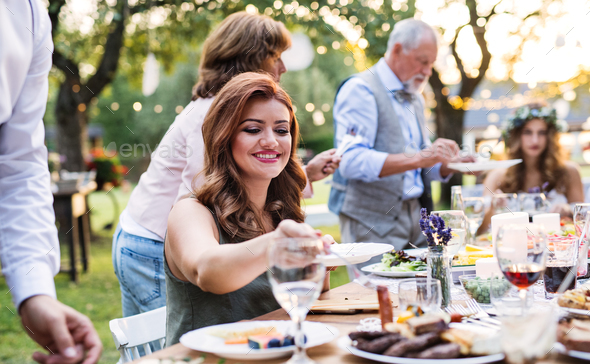 Guests eating at the wedding reception outside in the backyard. Stock Photo by halfpoint