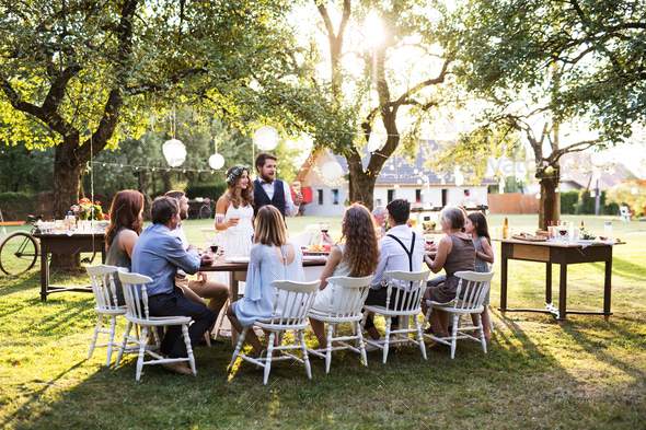 Bride and groom with guests at wedding reception outside in the backyard. Stock Photo by halfpoint