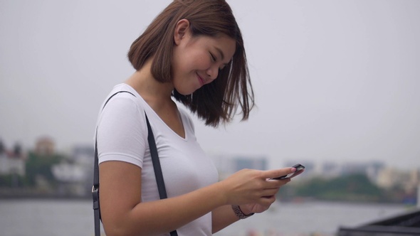 Beautiful young Asian woman using smartphone enjoying reading social media.