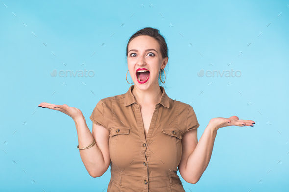 Surprised young woman shouting over blue background. Looking at camera Stock Photo by Satura_