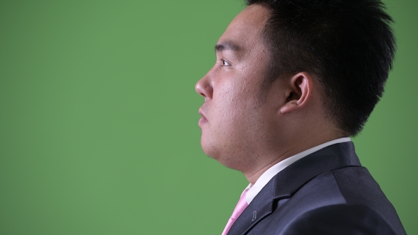 Young Handsome Overweight Asian Businessman Against Green Background