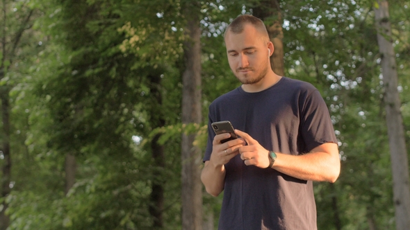 Man with a Phone and Wireless Headphones Listening To Music