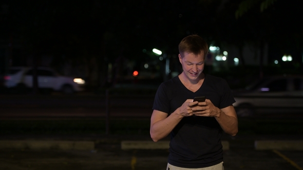 Young Handsome Scandinavian Man Using Phone in the Streets at Night alt