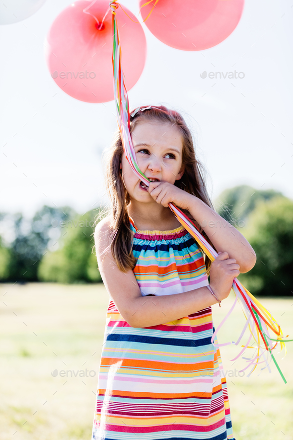 Little girl chewing balloon strings in her mouth Stock Photo by photocreo