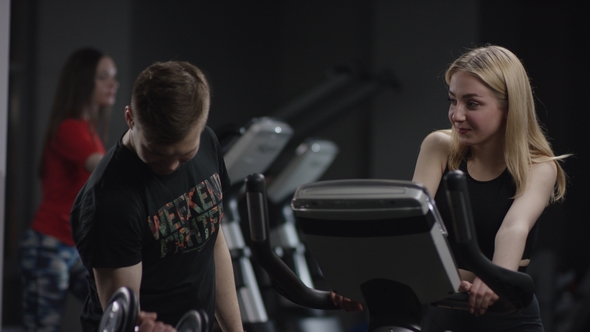Girl in Black Sport Wear doing Exercise Bike and Guy Comes To Show his arms