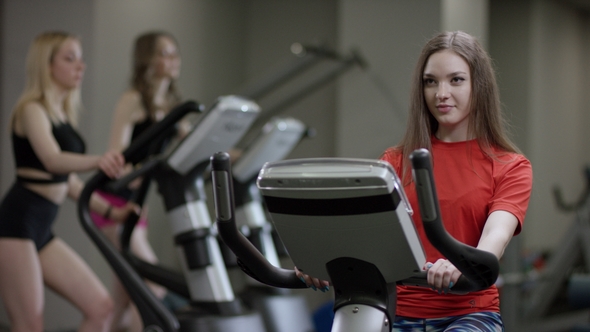 Lovely Girl in Red Shirt Vigorously Works on Exercise Bike and Just Working in the New Gym Against