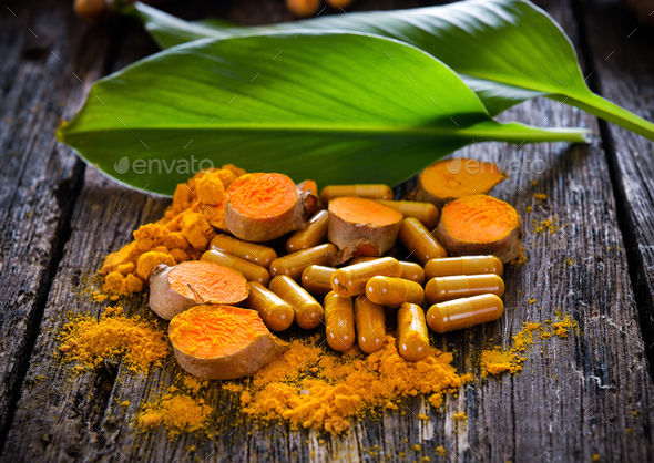 Turmeric powder and turmeric capsules on wooden background