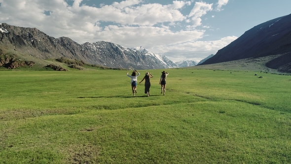 Group Of Friends Hold Hands And Run Away From Camera Toward Mountain alt
