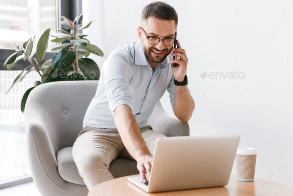 Photo of european man 30s in white shirt sitting in armchair and Stock Photo by vadymvdrobot