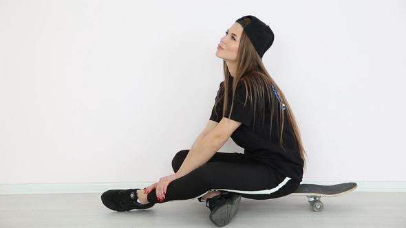 Teenage Girl in Trendy Hip Hop Clothes and Cap Posing Against White Wall with Skateboard
