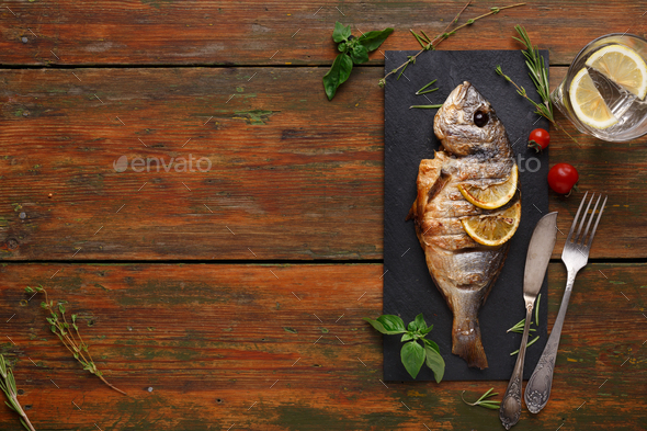Whole grilled dorado with lemon slices on wood - Stock Photo - Images