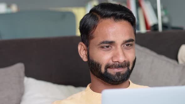 Happy Indian Man Sitting at Home on Sofa Using Laptop Computer alt