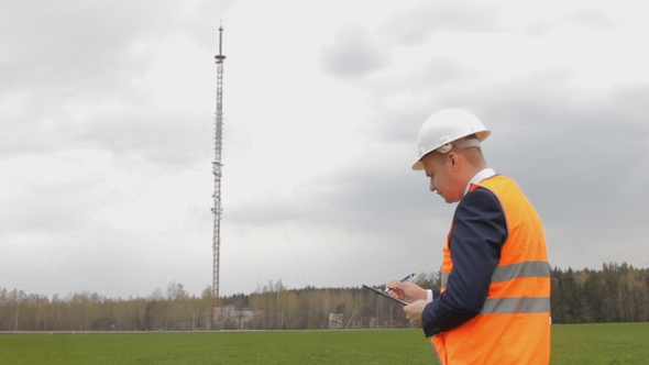 A Man in a Signal Jacket and Helmet Writes Notes in the Tablet, in the Background a Telephone Mobile alt