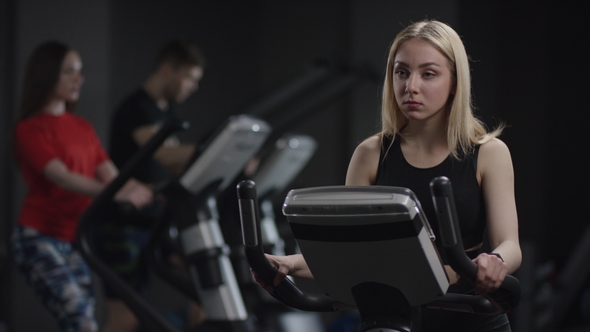 Girl in Black Sport Clothes Works Out on a Bike at Gym