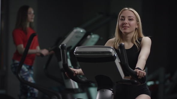 Lovely Girl in Blak Sport Wear Vigorously Works on Exercise Bike and Doesn't Approve Showing Thumbs