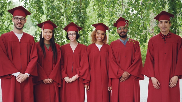 Portrait of Multiethnic Group of Graduating Students Standing Outdoors Wearing Red Gowns and Mortar alt