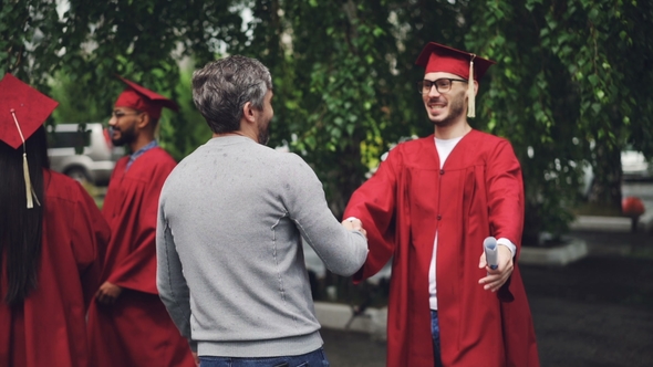Smiling Graduating Student Is Shaking His Father's Hand and Hugging Him