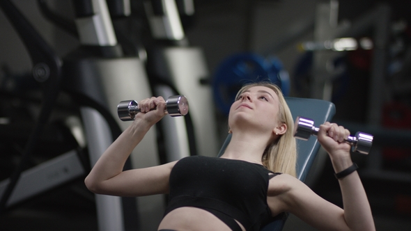 Cute Blonde Girl with Straight Hair in a Black Sport Wear with Blue Eyes Does a Dumbbell Press on an alt