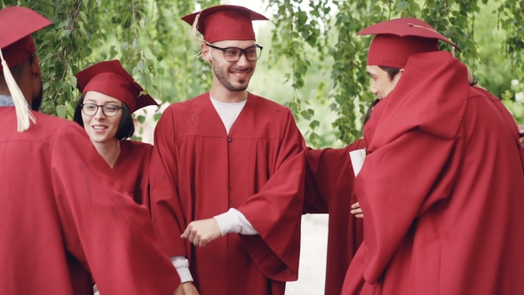 of Happy Graduates Wearing Gowns and Mortar-boards Hugging, Laughing and Congratulating Each Other alt