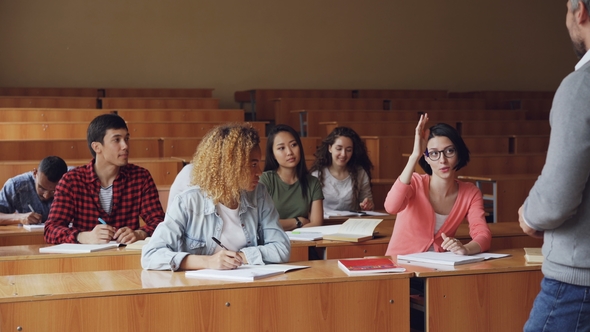 Pretty Young Woman Diligent Student Is Talking To High School Teacher Sitting at Desk While Other alt