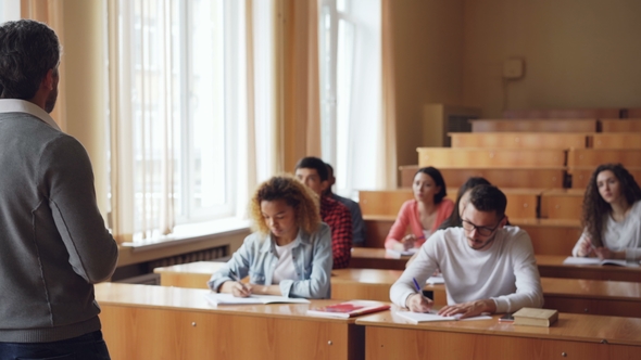 Bearded Man Professor Is Reading Lecture Talking and Gesturing While Students Are Listening and alt
