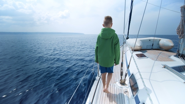 Little Boy Stands on the Bow of the Yacht and Shows the Way alt
