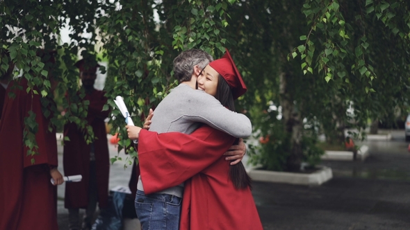 Loving Father Is Congratulating His Daughter on Graduation Day, People Are Hugging and Laughing alt