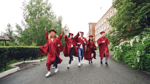 Dolly Shot of Excited Grads Running on Campus Wearing Gowns and Traditional Hats Celebrating End of alt