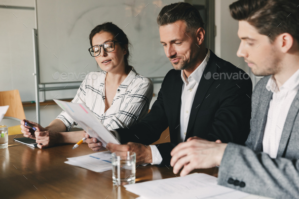 Group of business people in formal suits sitting at table in off Stock Photo by vadymvdrobot