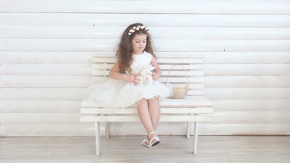 Cute Little Girl Sitting on a Bench and Playing with Plush Toys