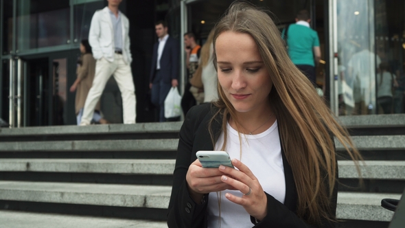 Business Woman Using Smartphone Near Entrance To City Building, People Go Behind