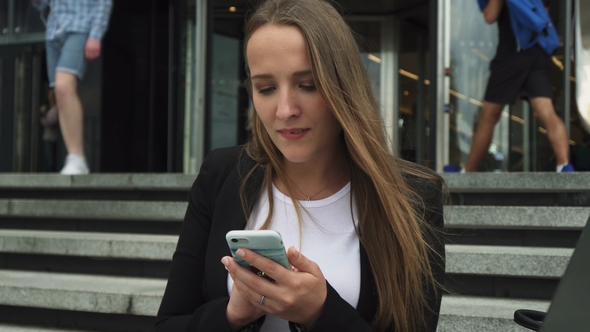Businesswoman Looking at Smartphone Screen Near City Building