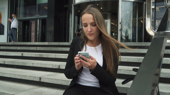 Business Woman Sitting on Steps of Urban Building and Using Smartphone