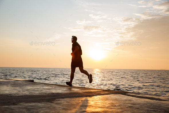 Image of muscular sporty man 30s in shorts and t-shirt running a Stock Photo by vadymvdrobot