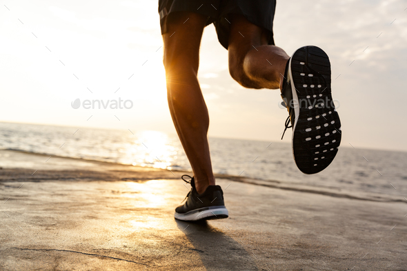 Cropped male legs of healthy sportsman wearing shorts and sneake Stock Photo by vadymvdrobot