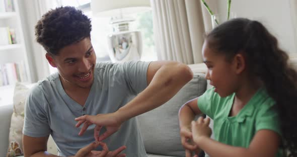 Happy biracial father and daughter sitting on sofa using sign language alt