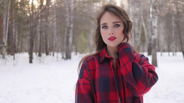 Young Woman with Wavy Hair Standing and Touching Face in Winter Forest