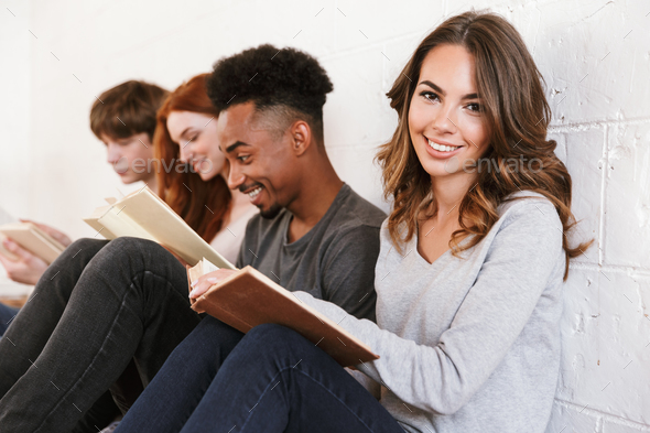 Friends students sitting over white wall. Focus on cheerful woman. Stock Photo by vadymvdrobot