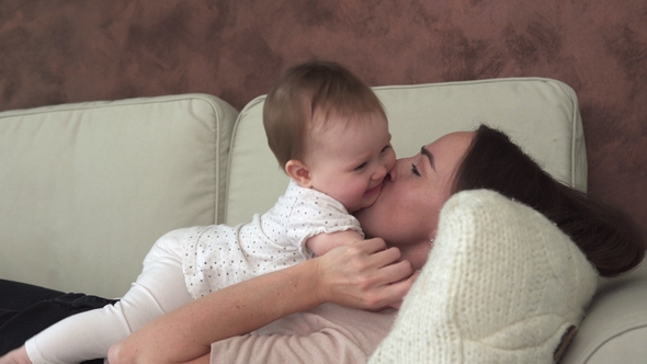 Mother Lies on Sofa and Kisses Little Adorable Baby