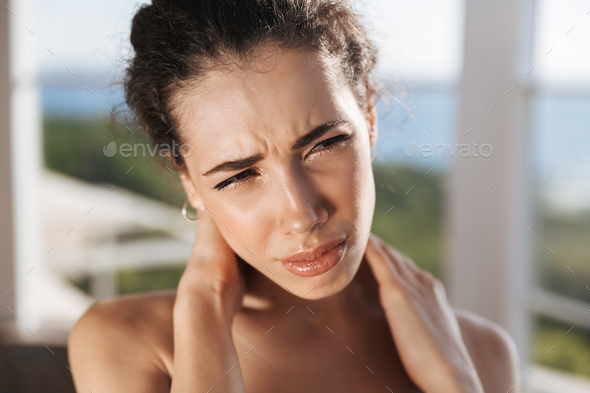 Upset young sportswoman having a neck pain Stock Photo by vadymvdrobot