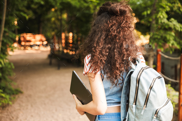 Photo from back of young brunette woman 18 20 wearing backpack