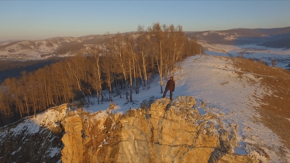 A Man Stands on the Edge of a Cliff and Enjoys the Sunset
