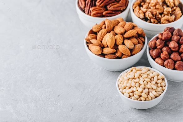 Pine nuts, almonds, pecans, walnuts and hazelnuts in white bowls on grey background. - Stock Photo - Images